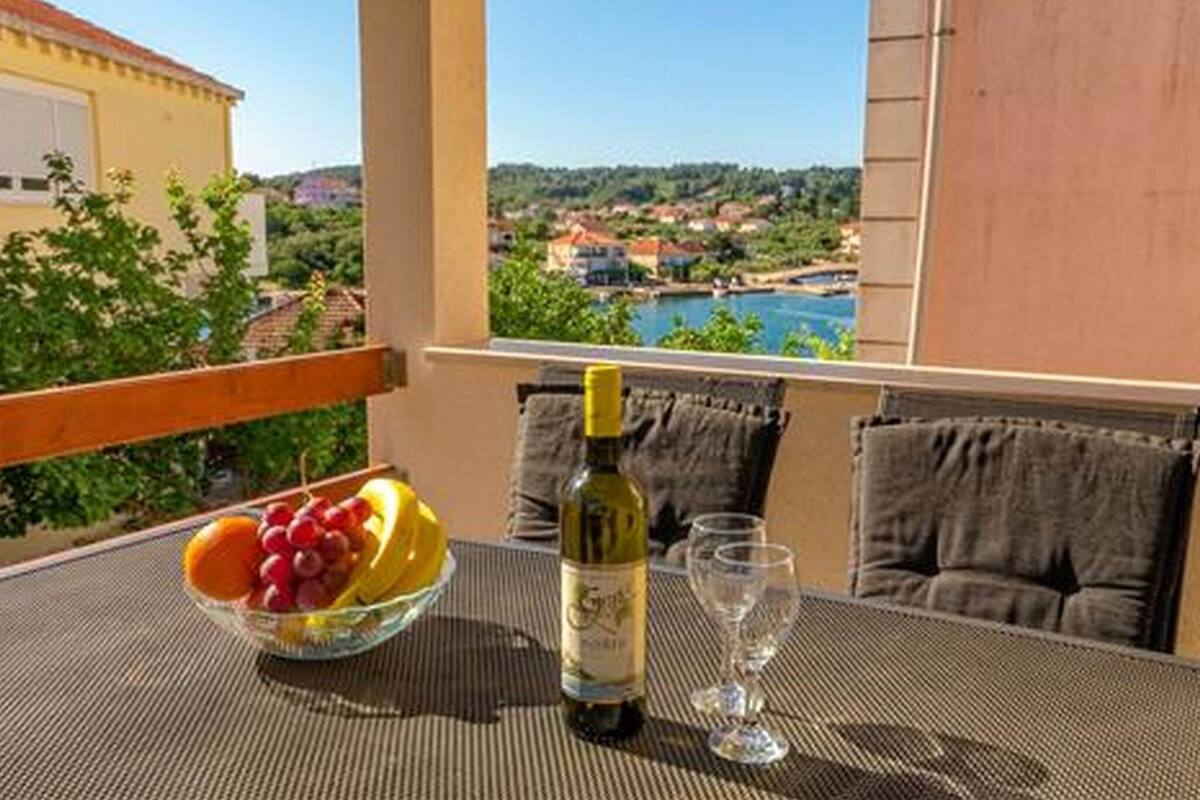 A balcony with a table, a bowl of fruit, a bottle of wine, and two glasses.