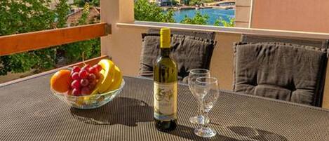 A balcony with a table, a bowl of fruit, a bottle of wine, and two glasses.
