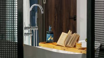A bathroom with a modern faucet, a bottle of whisky, and an open book on a wooden tray.