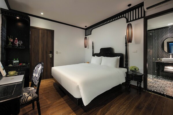 Un dormitorio moderno con una cama grande, suelo de madera, un escritorio con una silla, una mesita de noche con lámpara y un espejo.