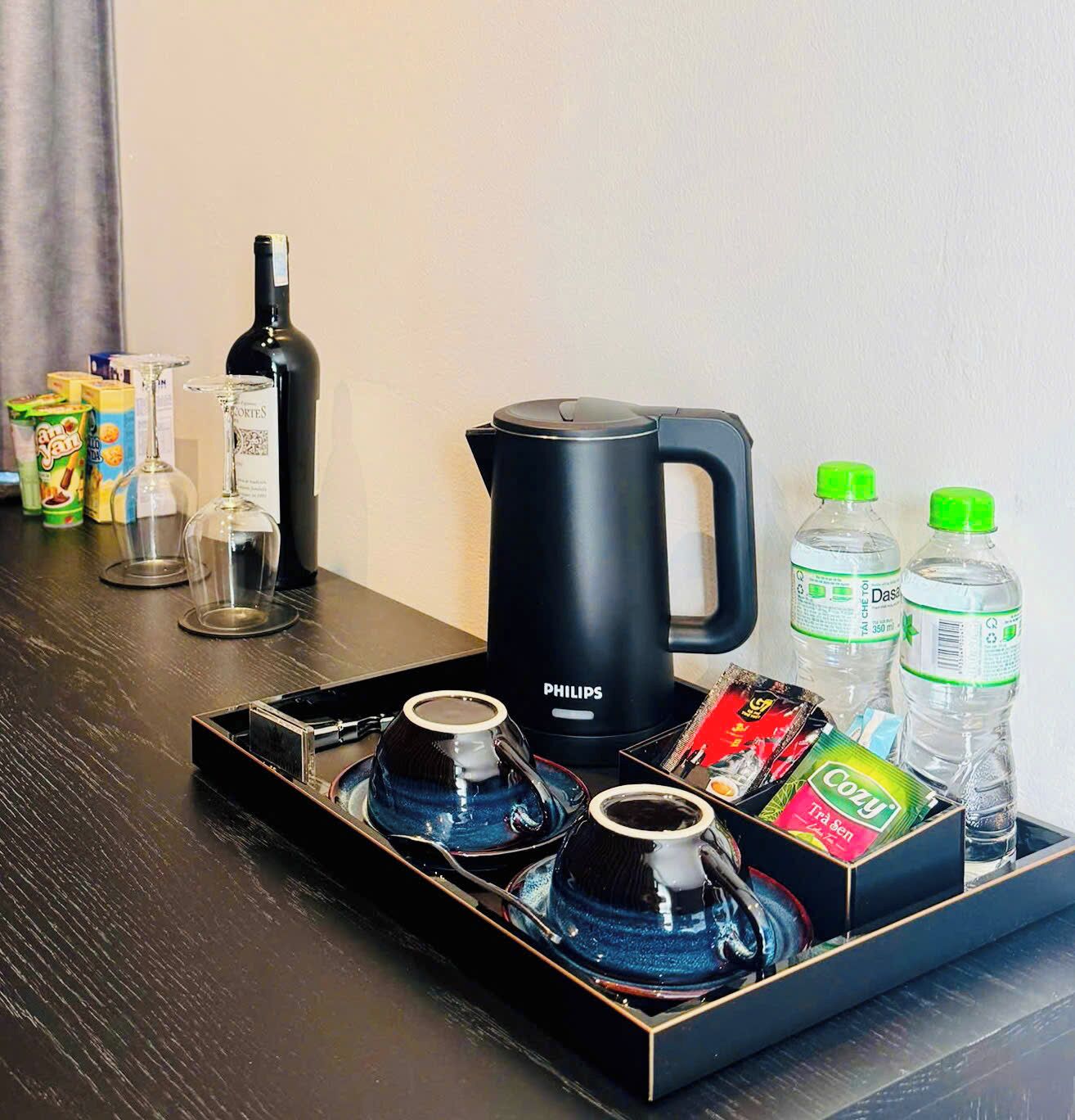 A tray with a coffee maker, two glasses, a bottle, and some snacks.