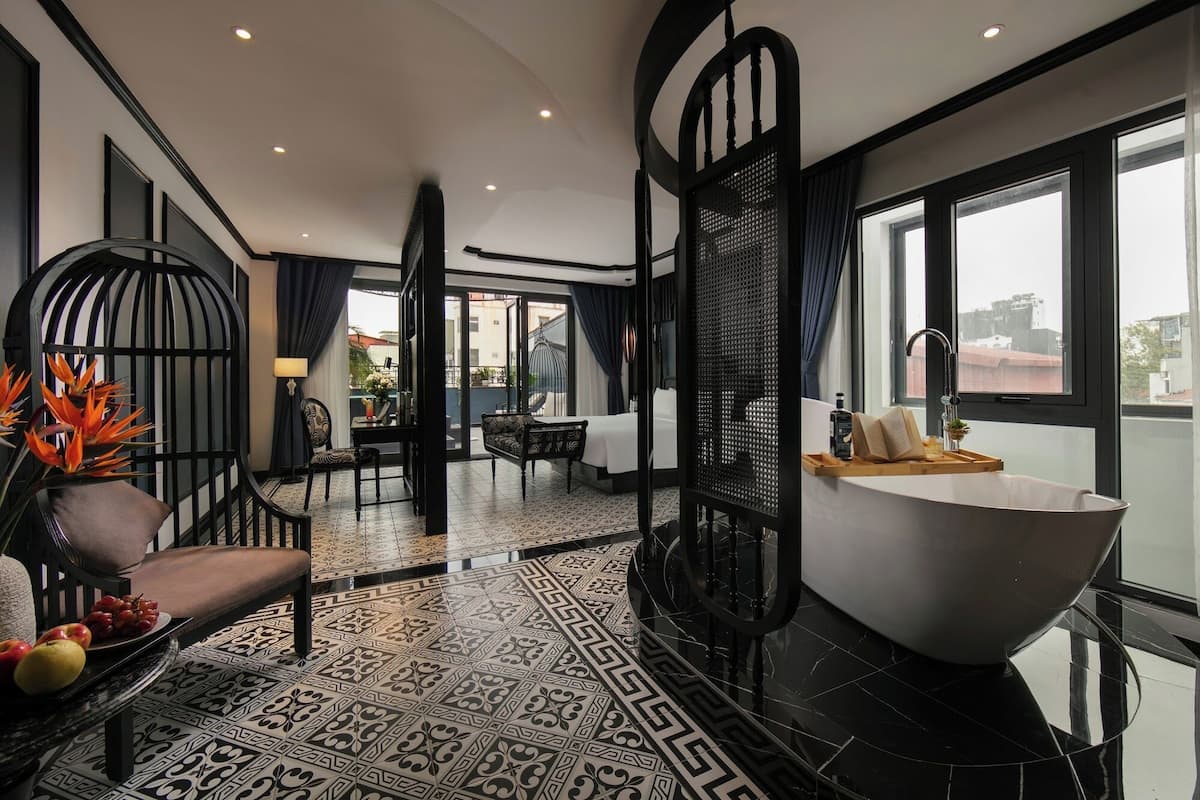 Una habitación de hotel moderna con una bañera grande, un comedor con mesa y sillas, y un balcón con vistas.