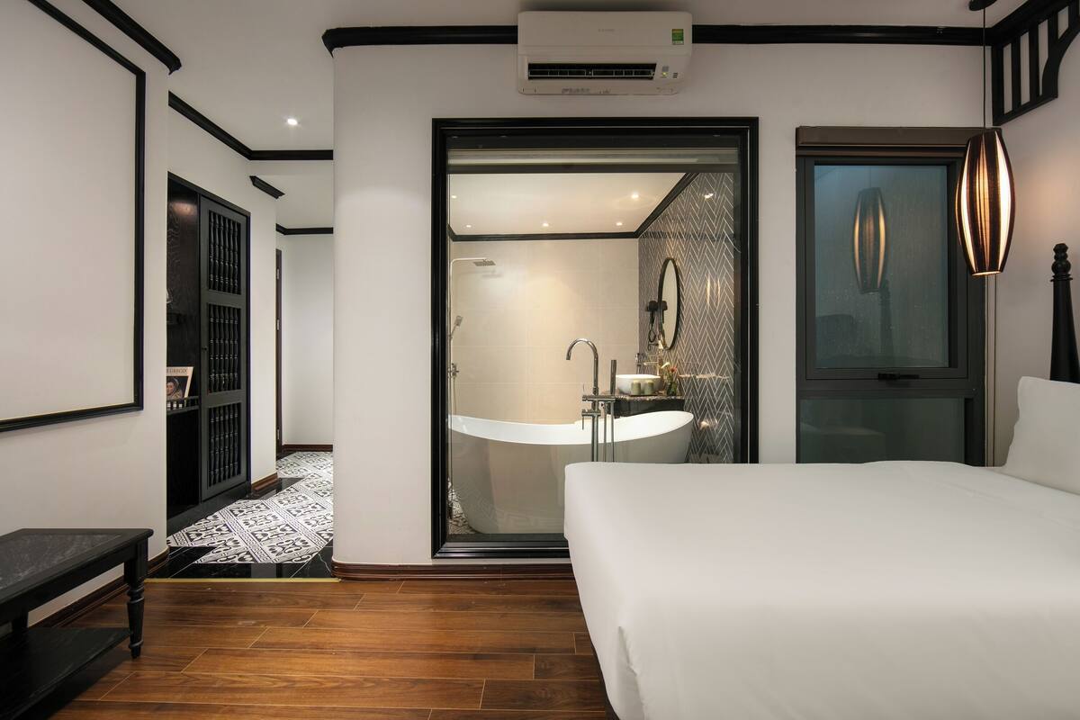 Una habitación de hotel moderna con una cama grande, un baño con bañera independiente y un ventanal amplio.