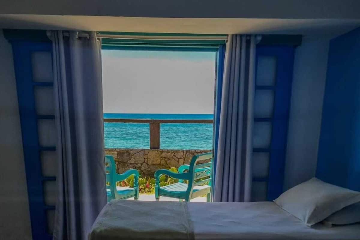 A hotel room with two beds, a view of the sea, and a balcony with chairs.