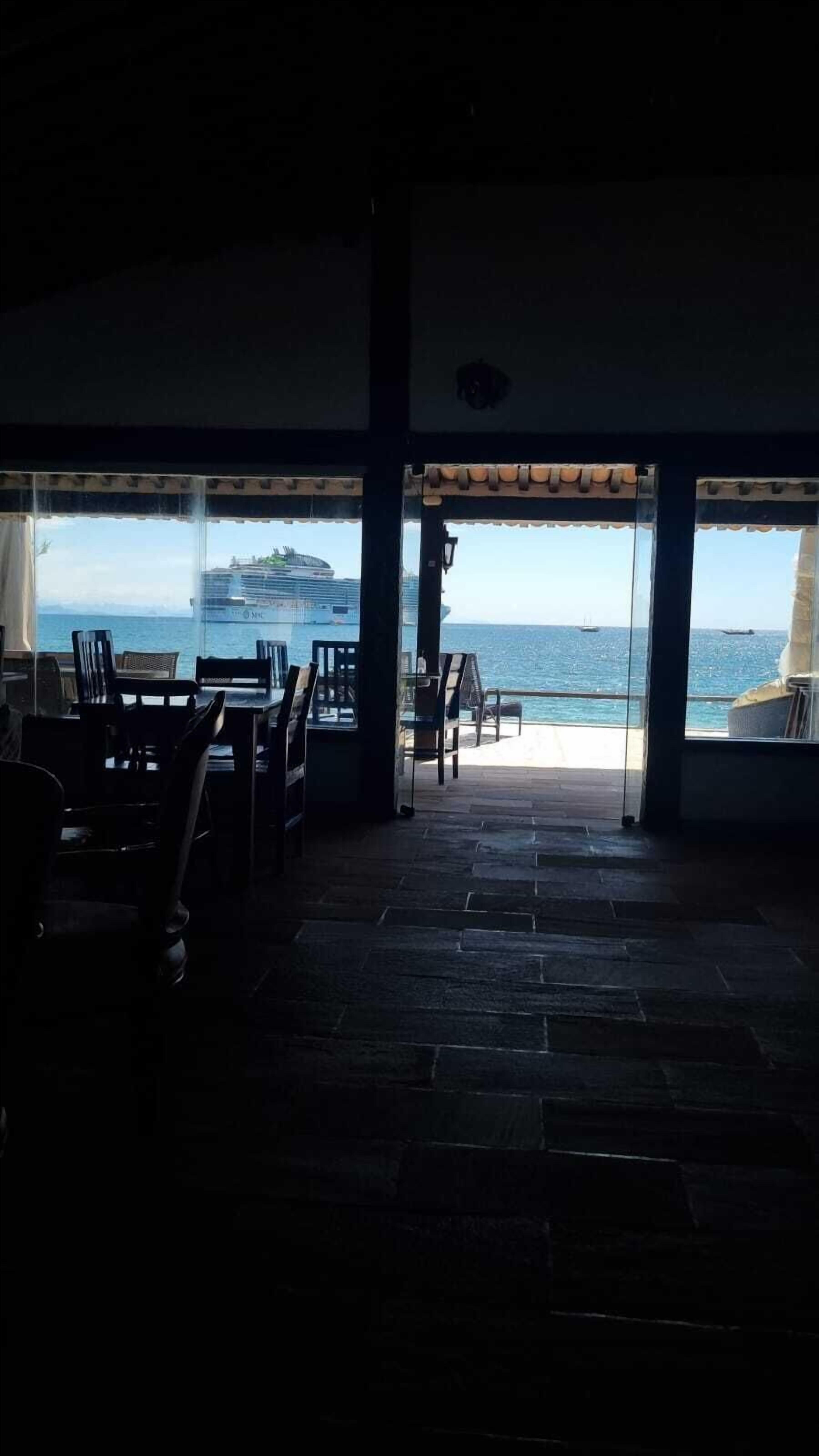 Zona de estar interior con vista al mar, con suelo de piedra y ventanas amplias.