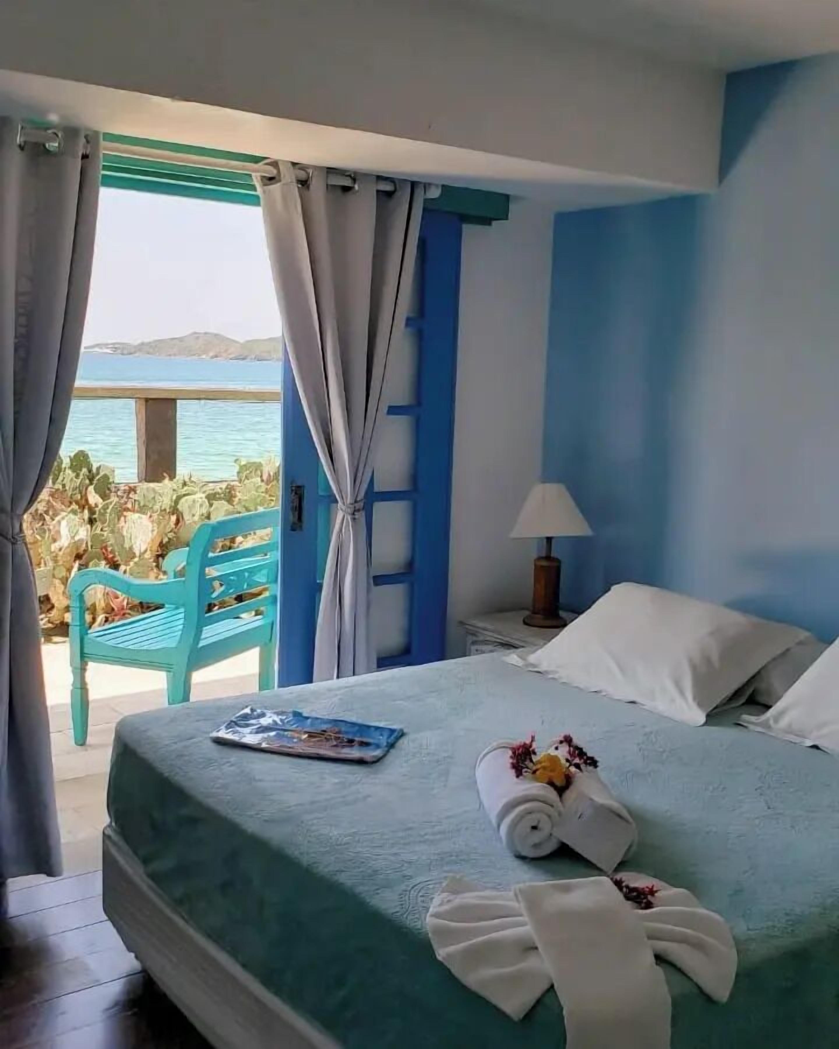 Un dormitorio con cama, mesita de noche, lámpara y vista al mar.