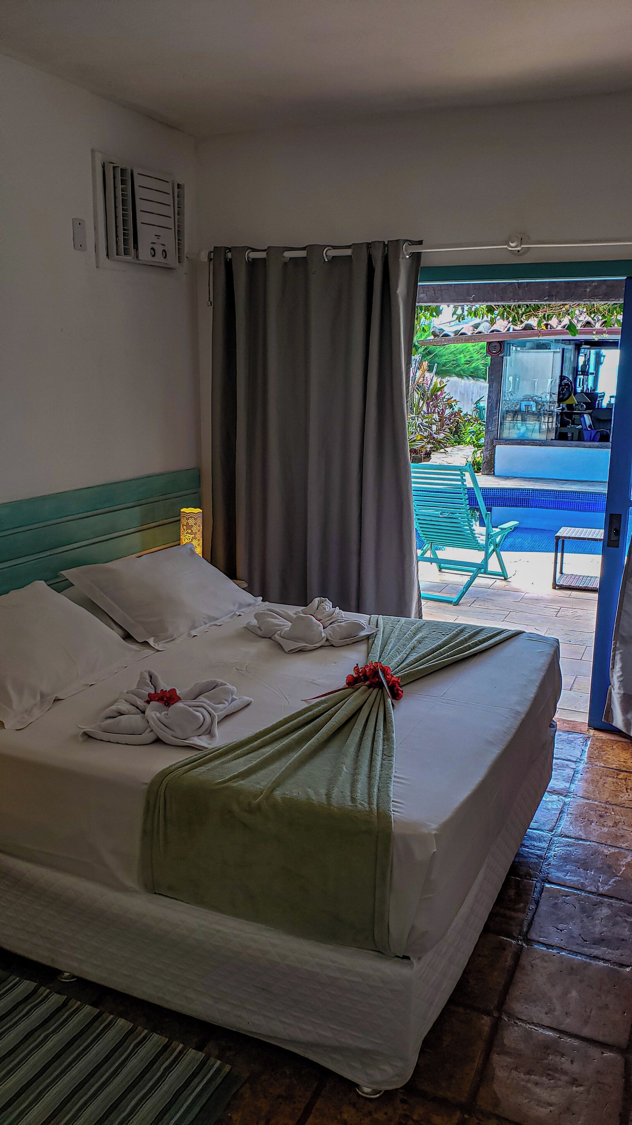 A hotel room with a neatly made bed, a bathroom with a shower, and a view of an outdoor pool area.
