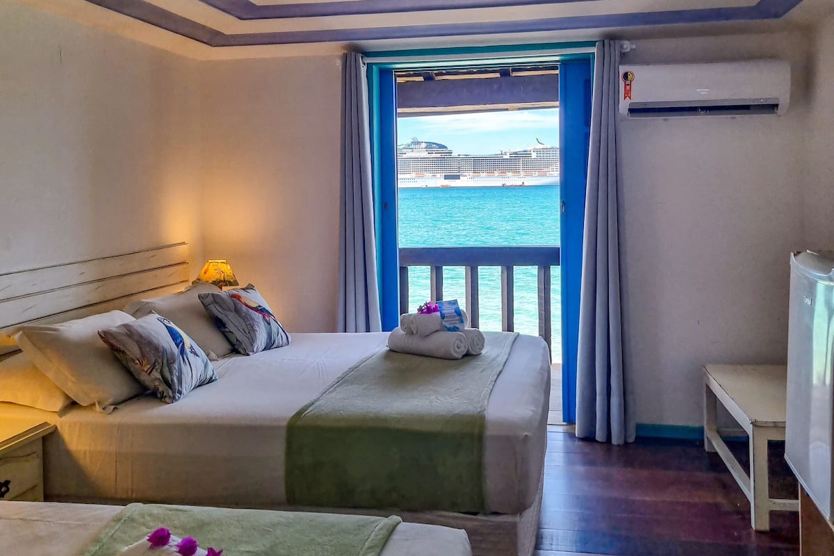 A hotel room with two beds, a ceiling fan, a view of the sea, and an air conditioning unit.