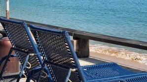 Vista al mar amb una cadira de platja i un para-sol, mar tranquil i una serralada de muntanyes a la distància.