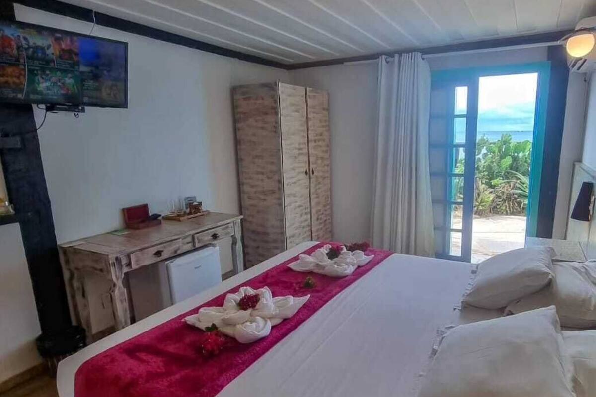 A hotel room with a bed, a desk, a television, and a view of the ocean.