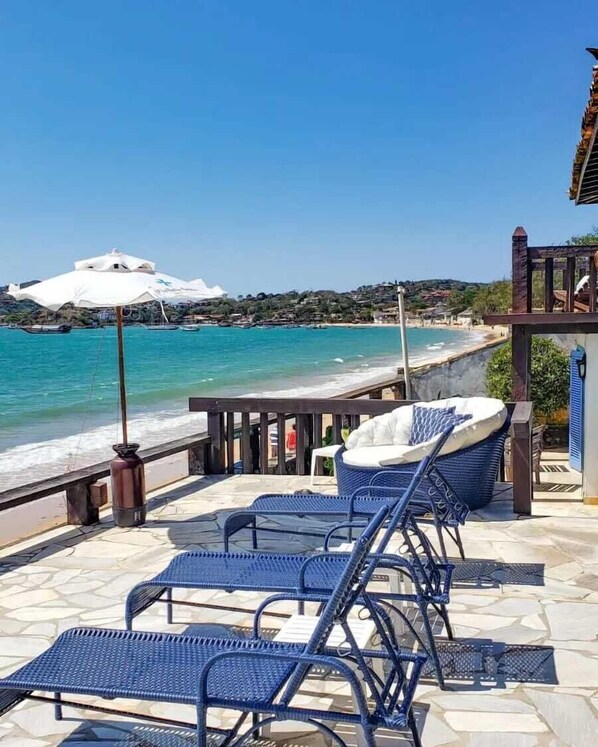 A seaside patio with wicker chairs and a white umbrella, overlooking a beach and turquoise waters. - Vila Bela-Emília (Búzios)