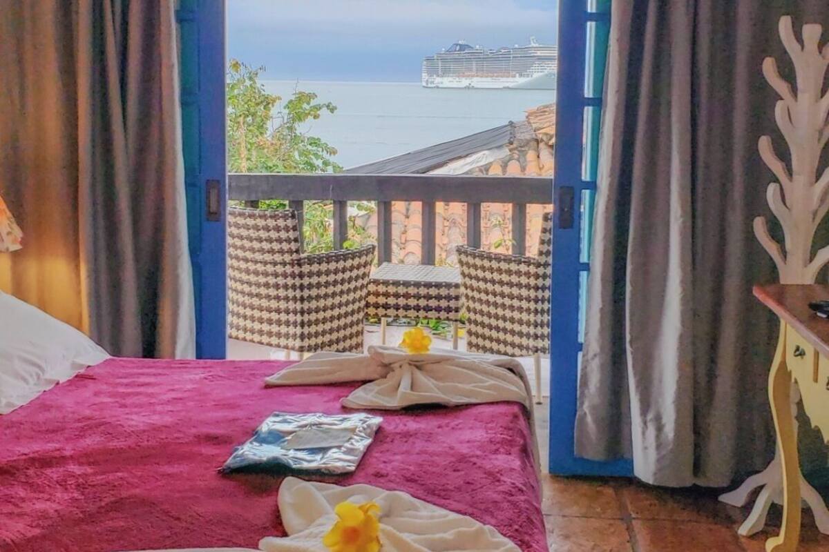 A hotel room with a bed, a view of the sea, and a balcony with chairs.