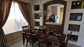 A dining area with a table set for four, surrounded by wooden chairs, a chandelier, and shelves with decorative items. - Spacious 7 Br, 4.5 Br Retreat With Pool 7 Bedroom Condo by RedAwning (Kissimmee)