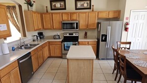 A kitchen with wooden cabinets, a central island, a microwave, a refrigerator, and a dining table with chairs. - Spacious 7 Br, 4.5 Br Retreat With Pool 7 Bedroom Condo by RedAwning (Kissimmee)