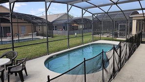 A covered outdoor swimming pool area with a fence, chairs, and a lawn. - Spacious 7 Br, 4.5 Br Retreat With Pool 7 Bedroom Condo by RedAwning (Kissimmee)