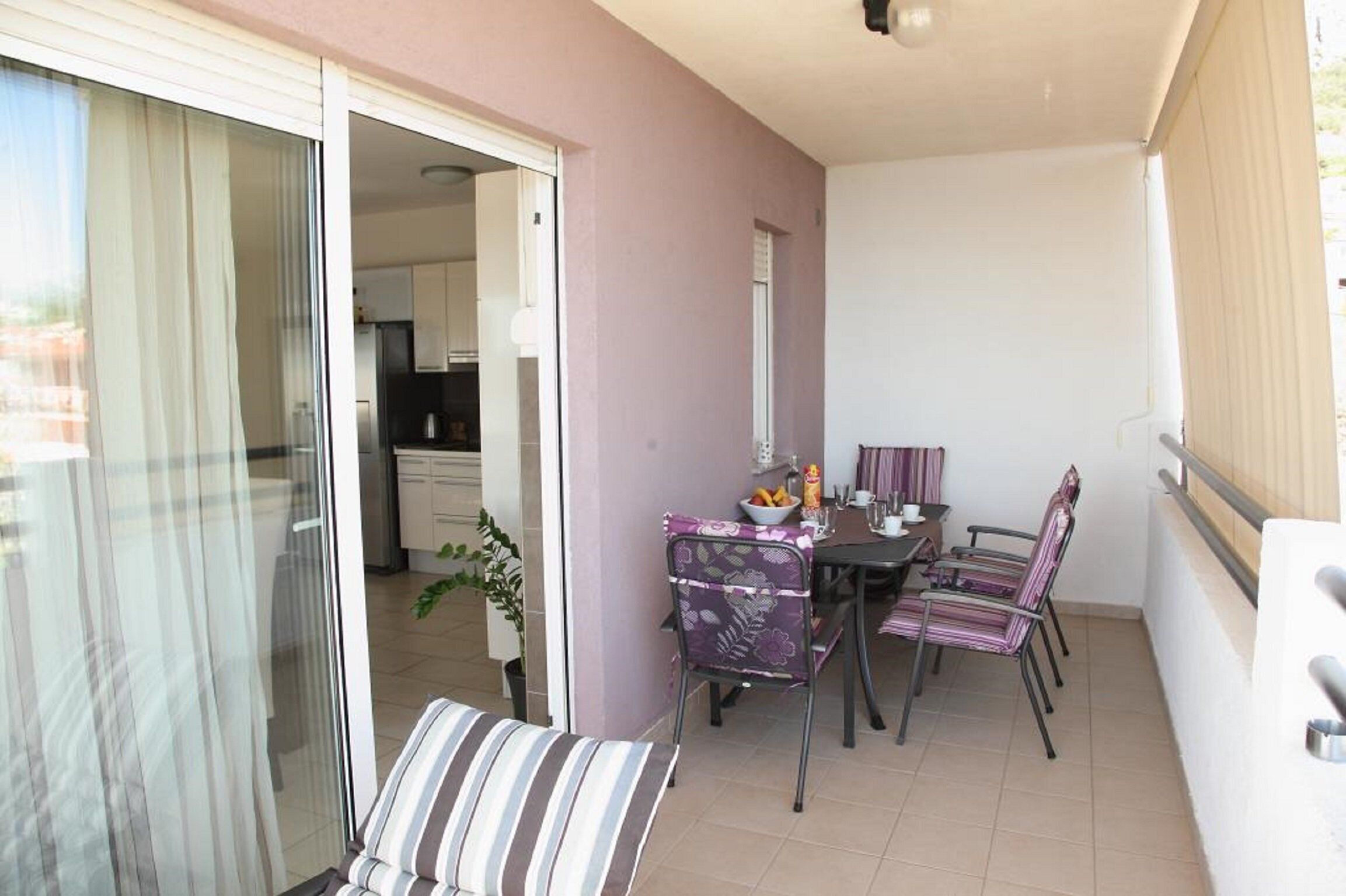A balcony with a dining table and chairs, a sliding glass door leading to a kitchen, and a potted plant.