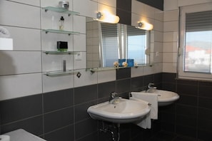 Een moderne badkamer met twee wasbakken, een grote spiegel en glazen planken met toiletartikelen.