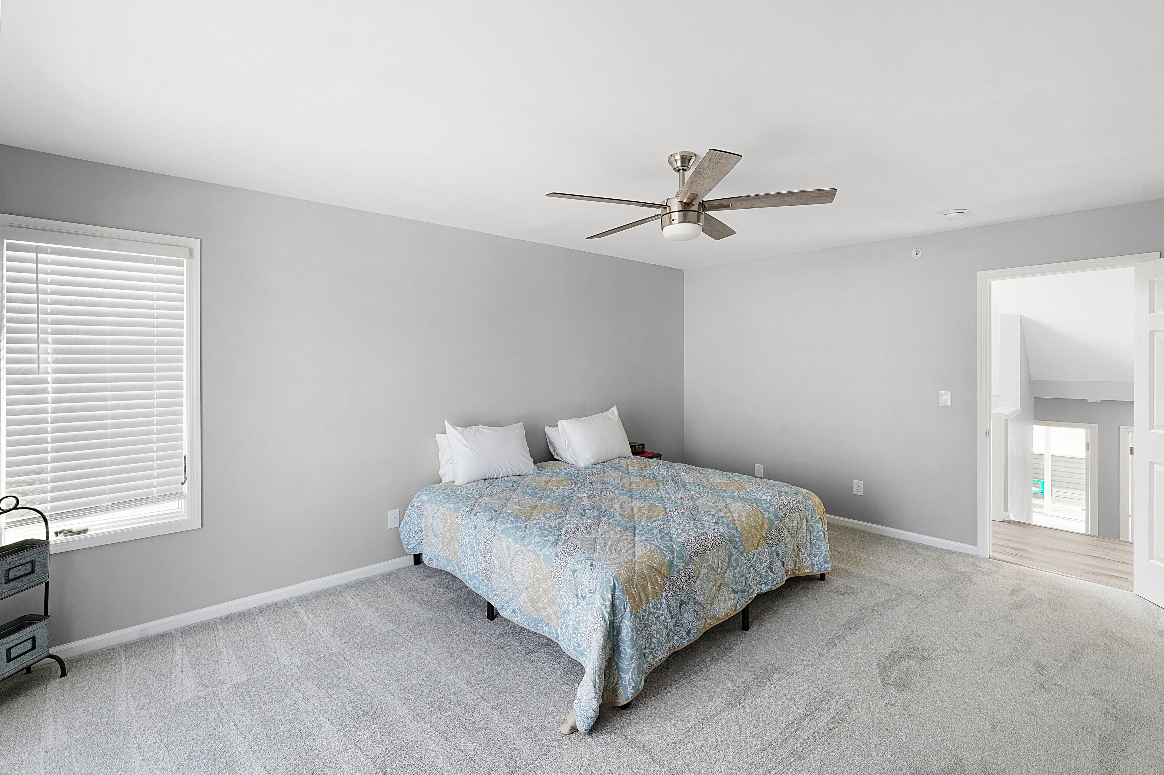 Une chambre à coucher avec un lit, un ventilateur de plafond et une fenêtre avec des stores.