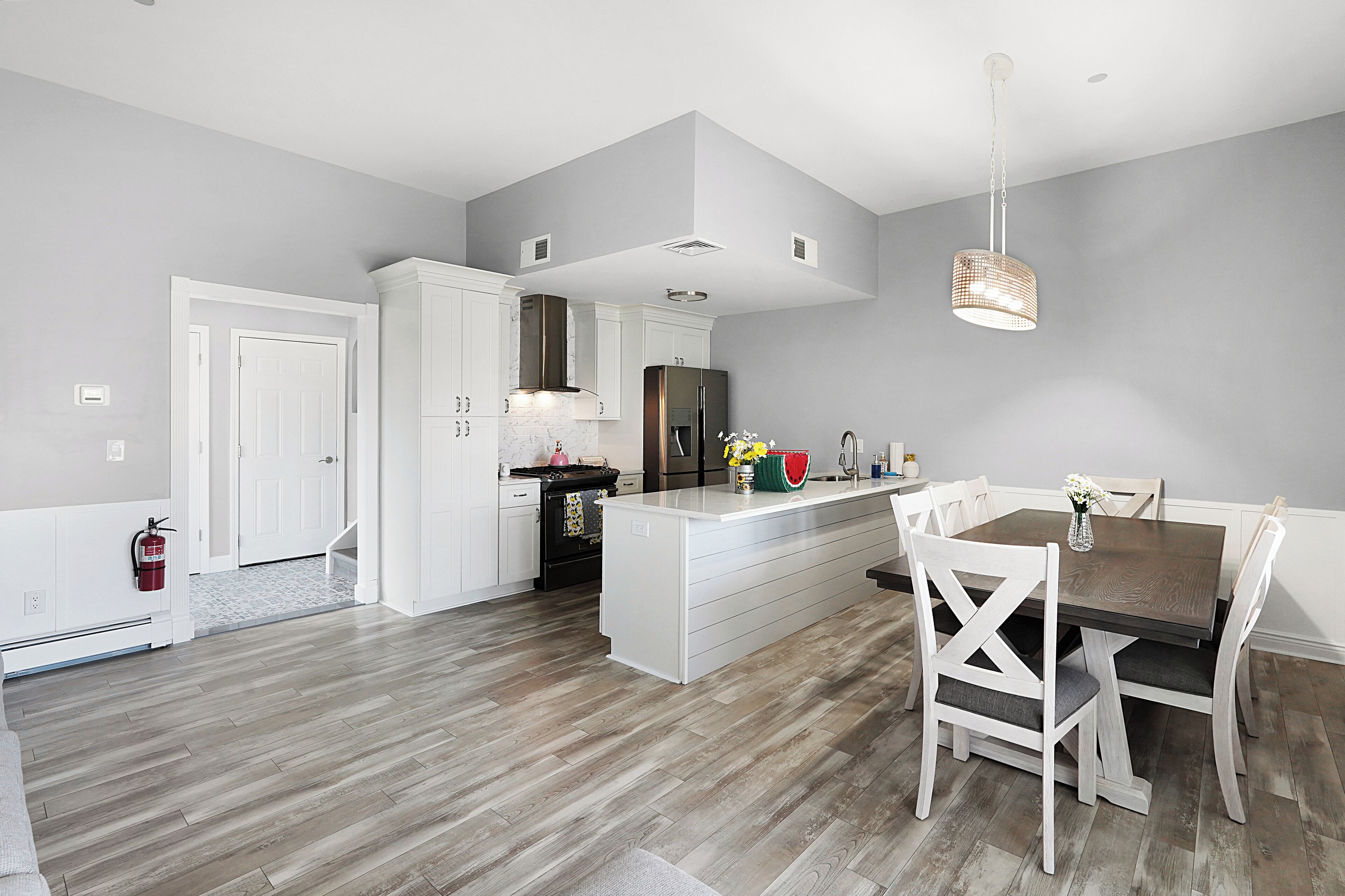 A modern kitchen with white cabinetry, a central island, and a dining area with white chairs.