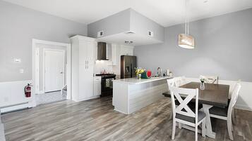 A modern kitchen with white cabinetry, a central island, and a dining area with white chairs.