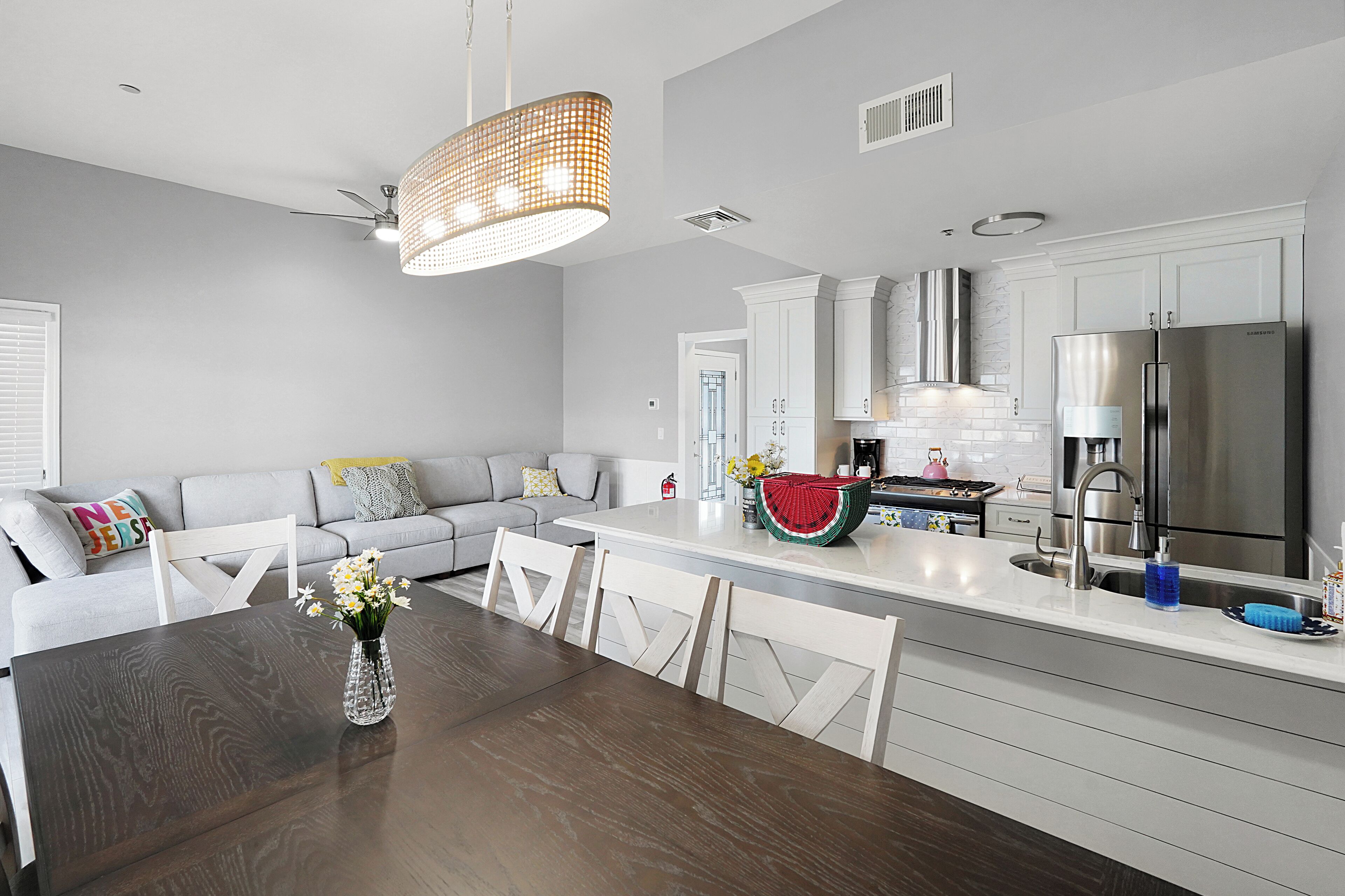 A modern kitchen with white cabinetry, a stainless steel refrigerator, and a dining area with a wooden table and chairs.