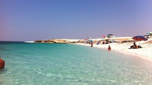 Ein Strand mit klarem türkisblauem Wasser, weißem Sand und mehreren Sonnenschirmen.