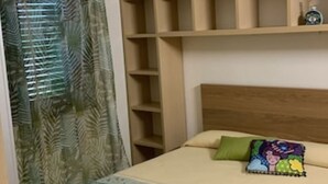 Une chambre à coucher avec un lit, une tête de lit, une étagère et une fenêtre avec des rideaux.