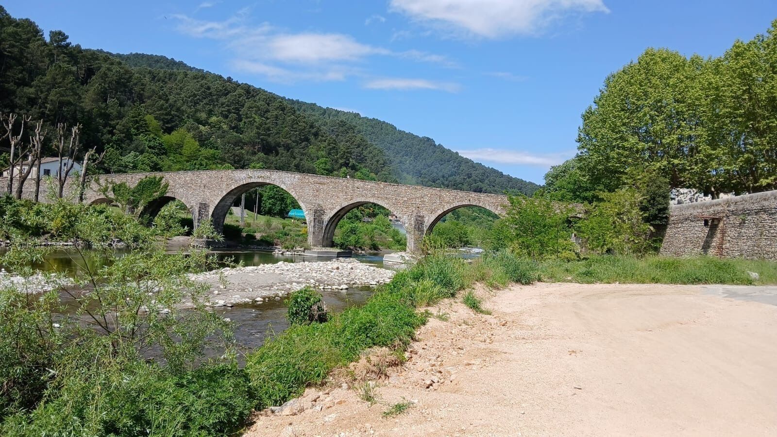 A stone bridge over a river, surrounded by greenery and hills.