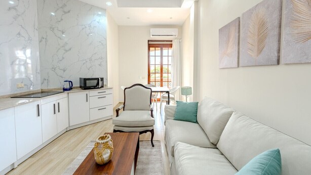 Una sala de estar moderna con un sofá blanco, una mesa de centro de madera y una cocina con armarios blancos y salpicadero de mármol.