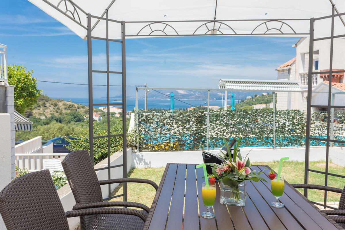 An outdoor dining area with wicker chairs and a table, overlooking a pool and a mountainous landscape.