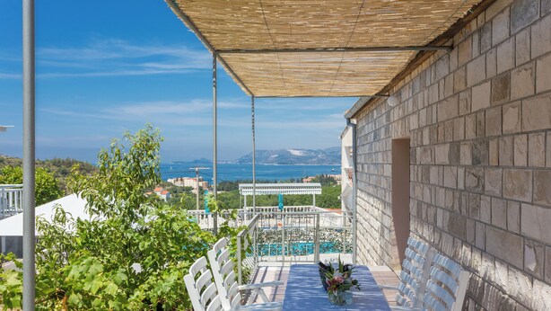 A terrace with a table and chairs, overlooking a pool and a mountainous landscape. - Apartments Oleander Sea View (Konavle)