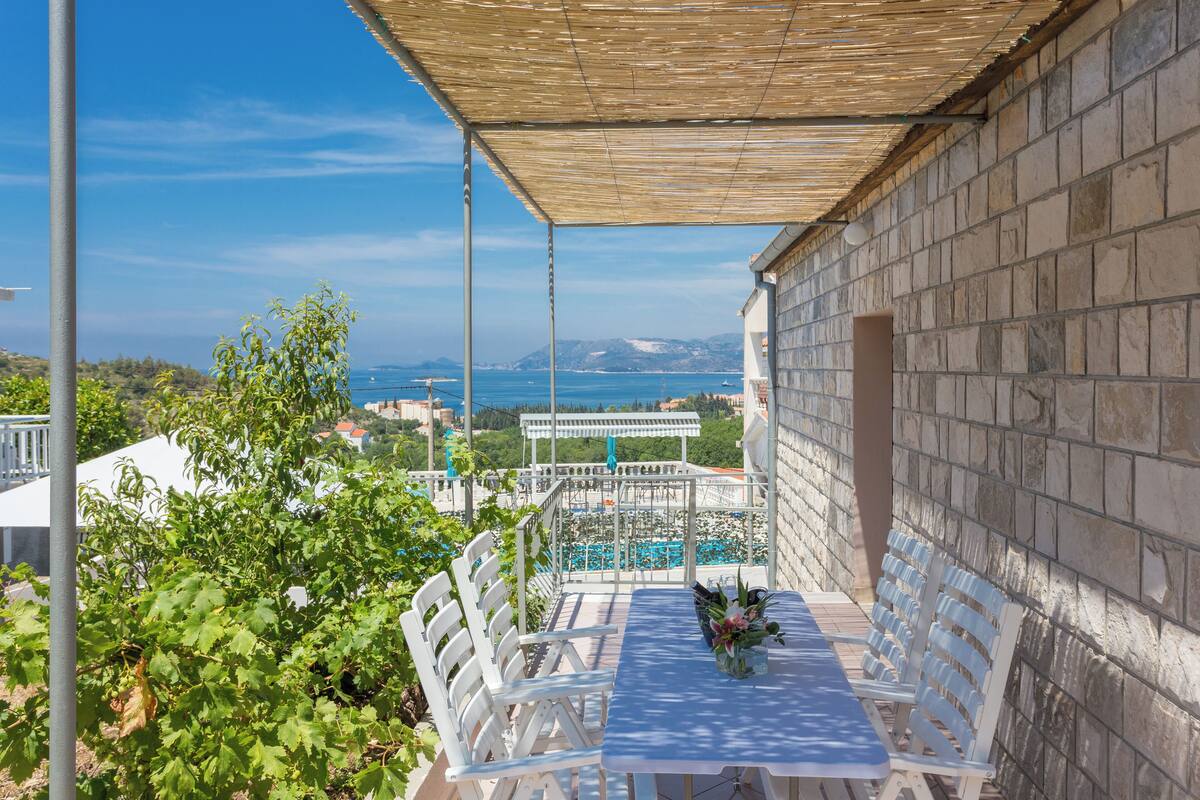 A terrace with a table and chairs, overlooking a pool and a mountainous landscape.