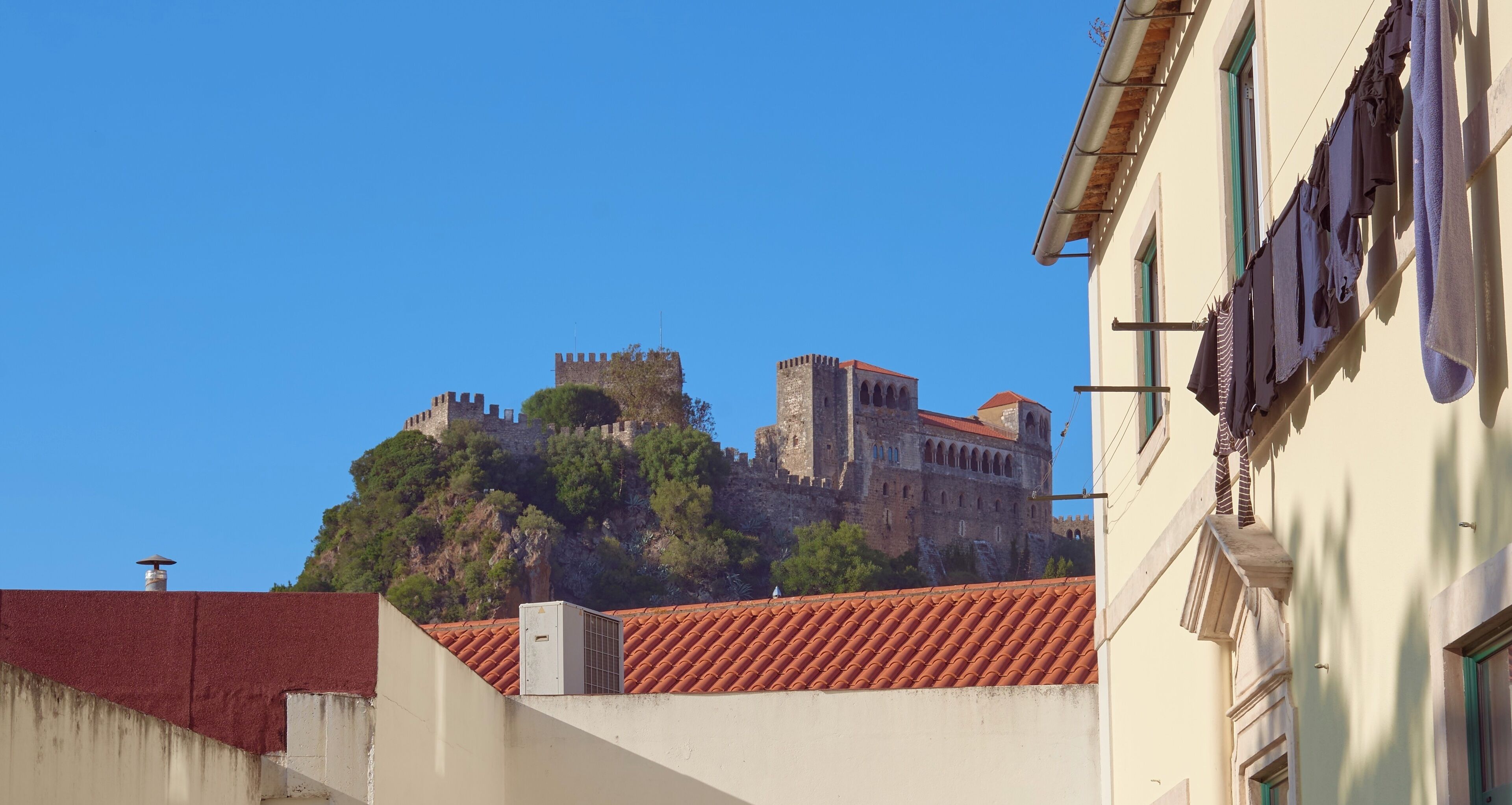 A historic castle on a hill with a red-tiled roof, overlooking a building with laundry hanging outside.