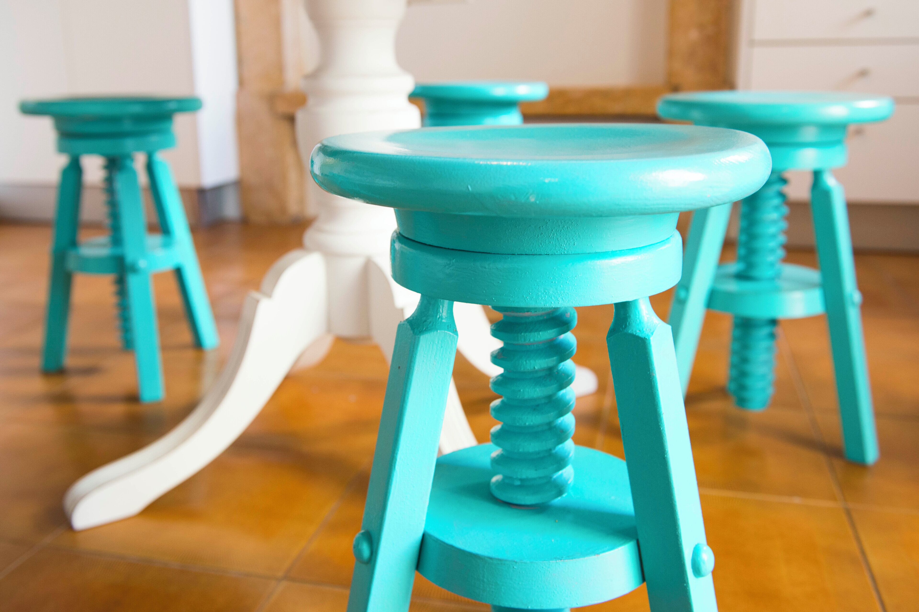 A close-up of turquoise stools with a white chair in the background.