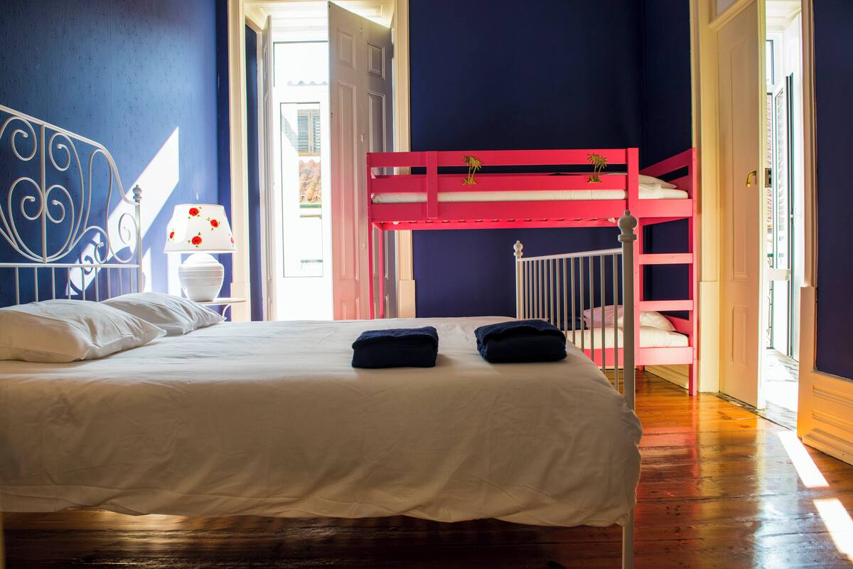 A room with a bunk bed, a single bed, and a nightstand with a lamp.