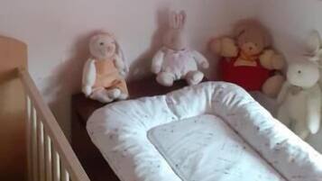 Ein Kinderzimmer mit einem Babybett, Kuscheltieren und einem an der Wand befestigten Regal mit einem Spielzeug.