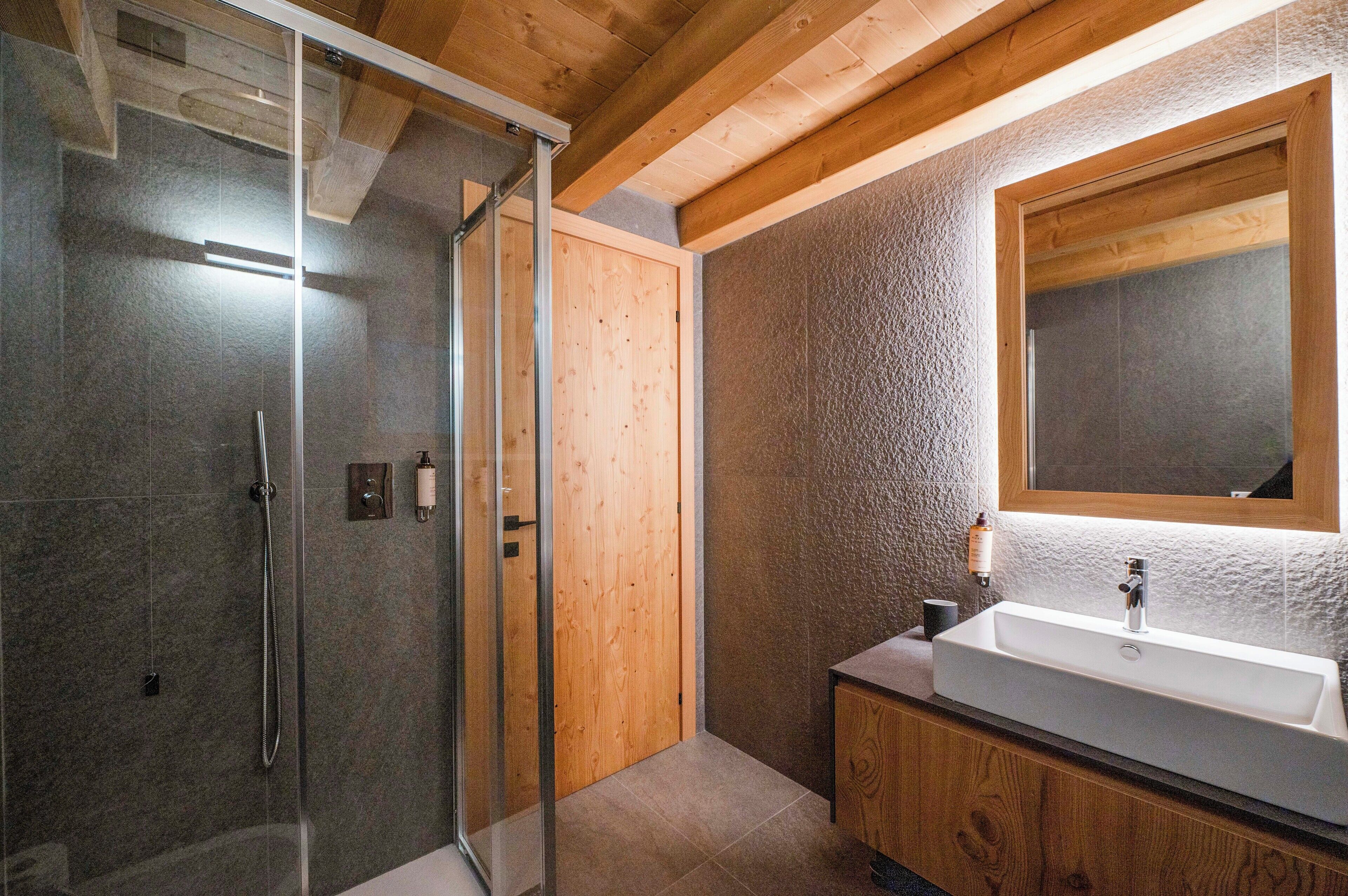 Une salle de bain moderne avec une douche en verre, des éléments décoratifs en bois et un grand miroir au-dessus d’un lavabo.
