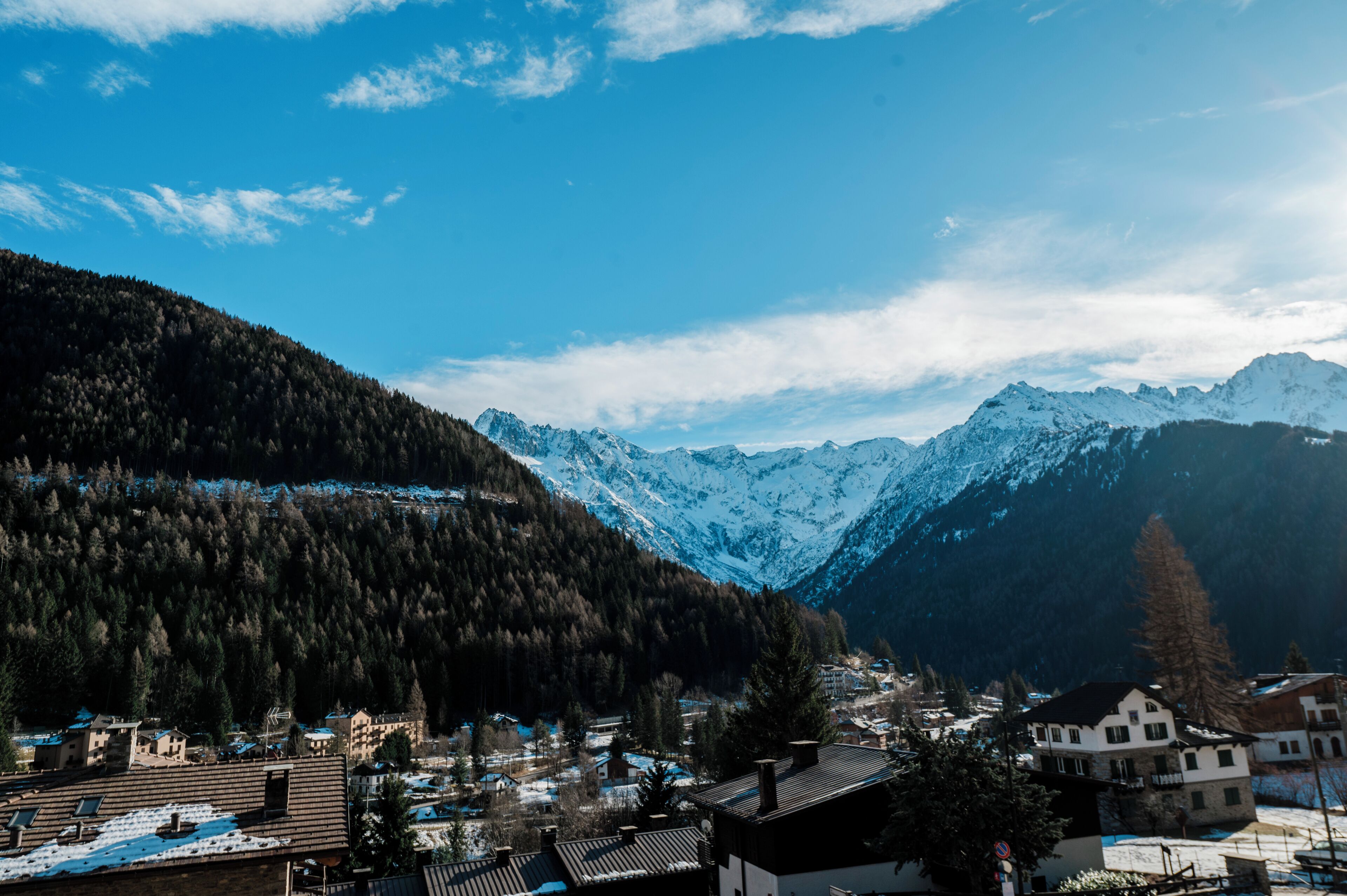 Een bergachtig landschap met besneeuwde toppen, een dorp met traditionele architectuur en een heldere blauwe lucht.