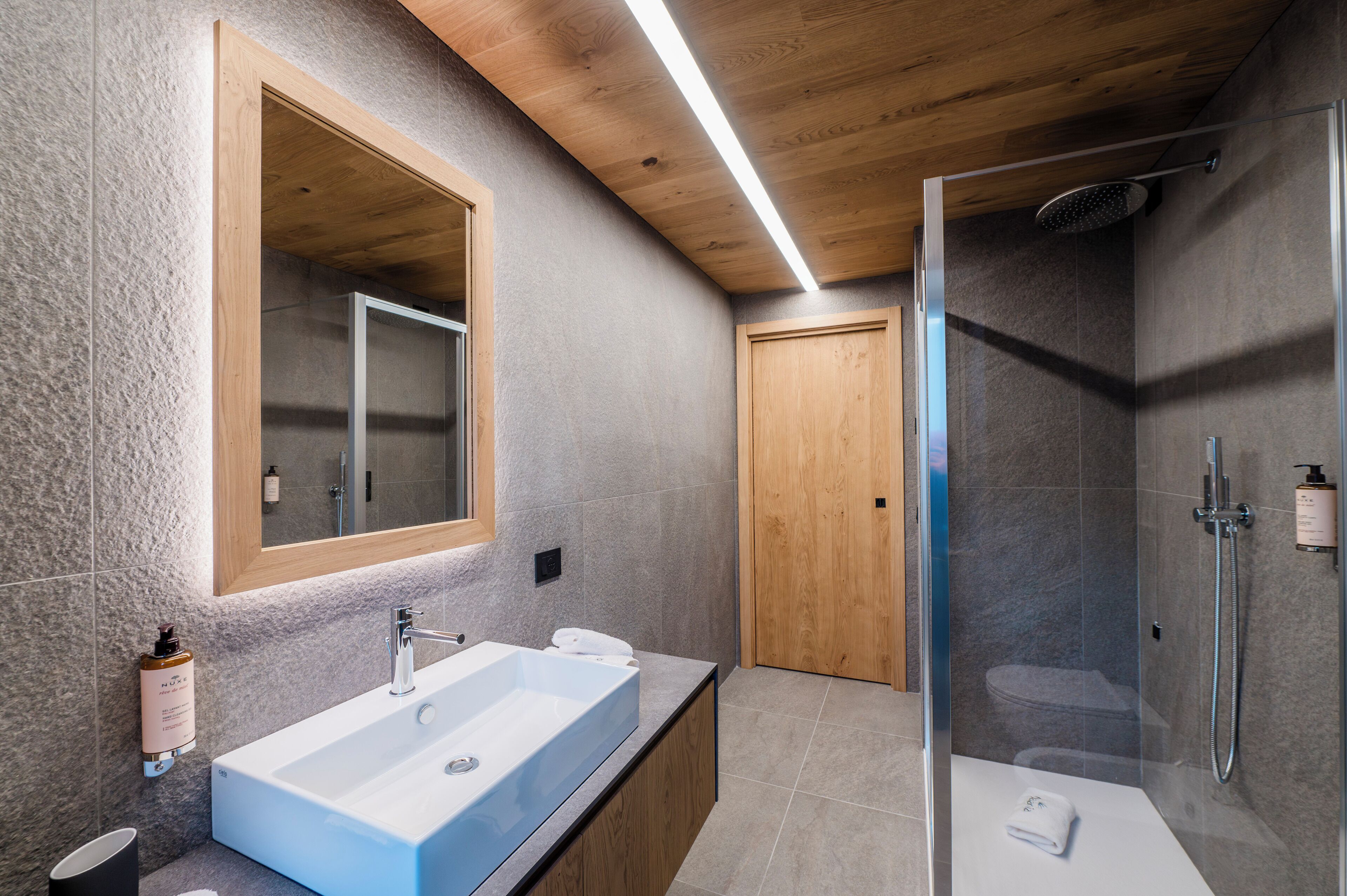 Un baño moderno con un espejo grande, una bañera independiente, un box de ducha y una puerta de madera.