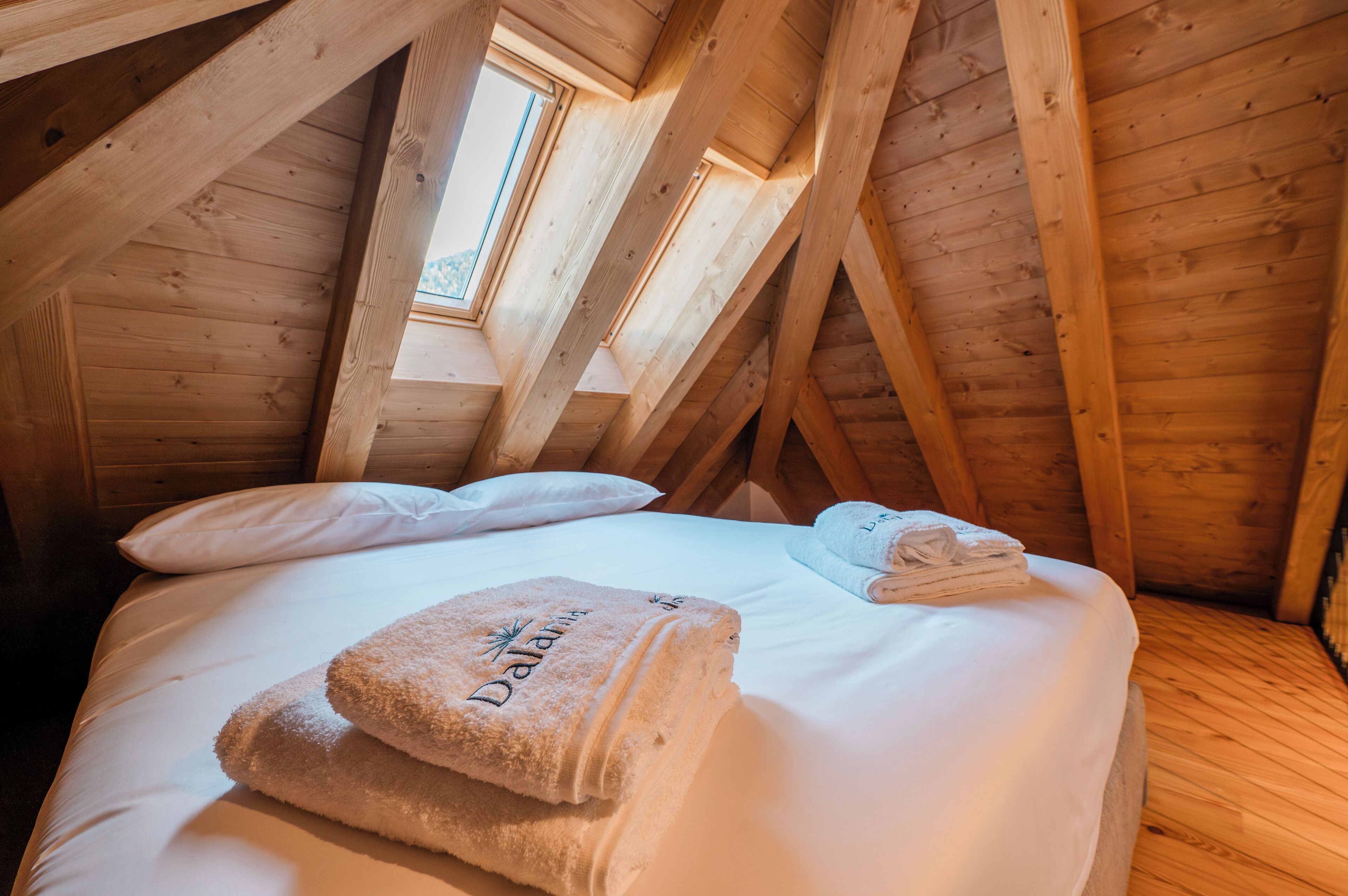 A wooden ceiling with skylights, a bed with white linens, and two towels on the bed.