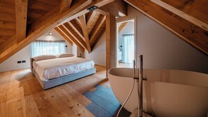 A bedroom with a wooden ceiling, a bed, a bathtub, and a view of a bathroom. - DALANIA MOUNTAIN APARTMENTS (Ponte di Legno)