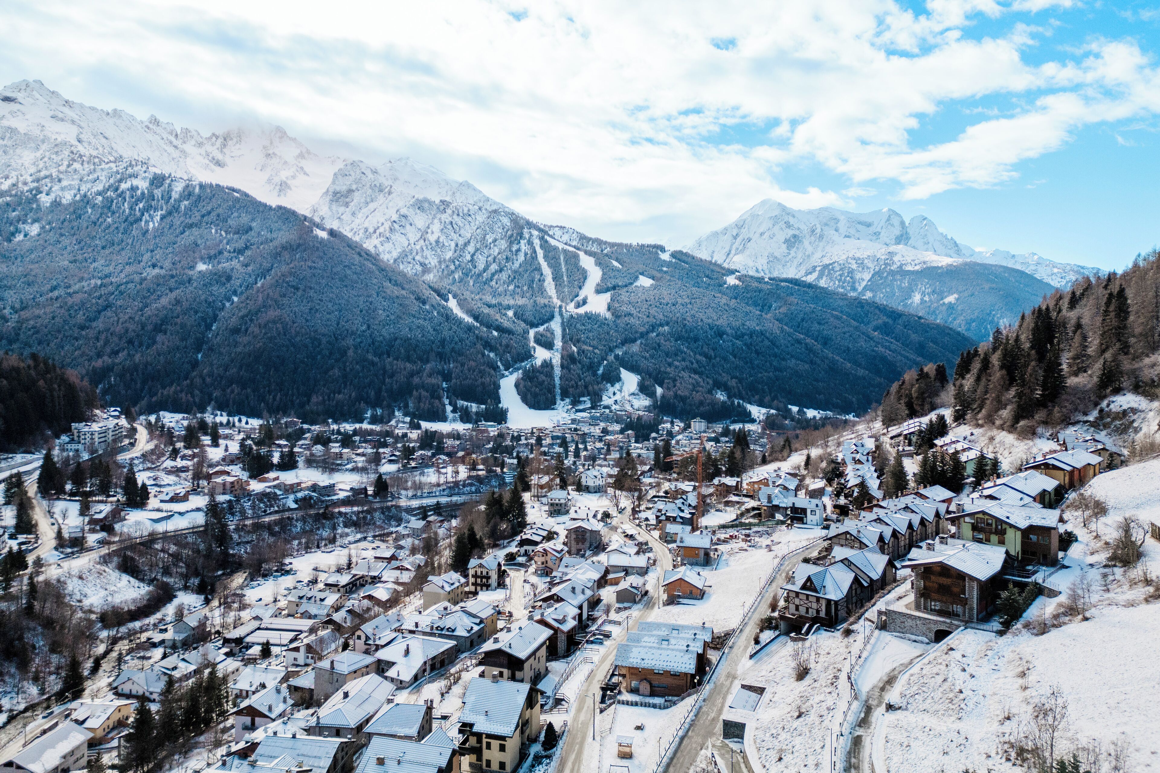 Pueblo cubierto de nieve con casas de madera tradicionales, una pista de esquí y una vista despejada de las montañas circundantes.