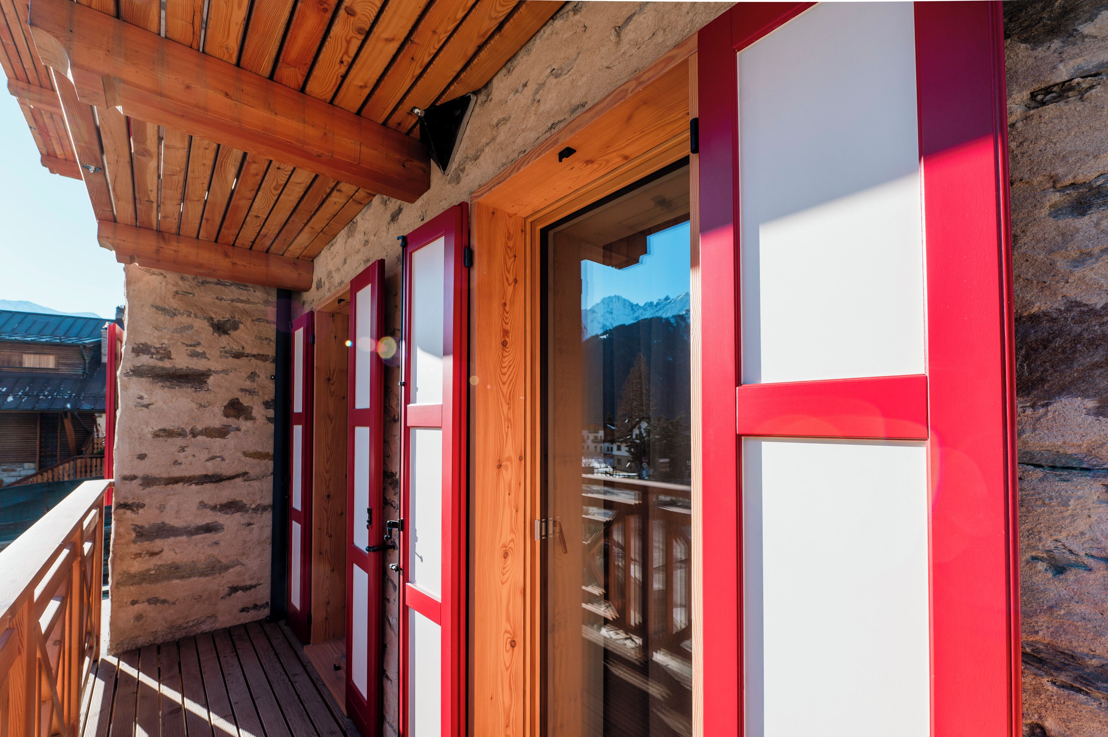 A wooden balcony with red-framed glass doors, a wooden ceiling, and a view of mountains.