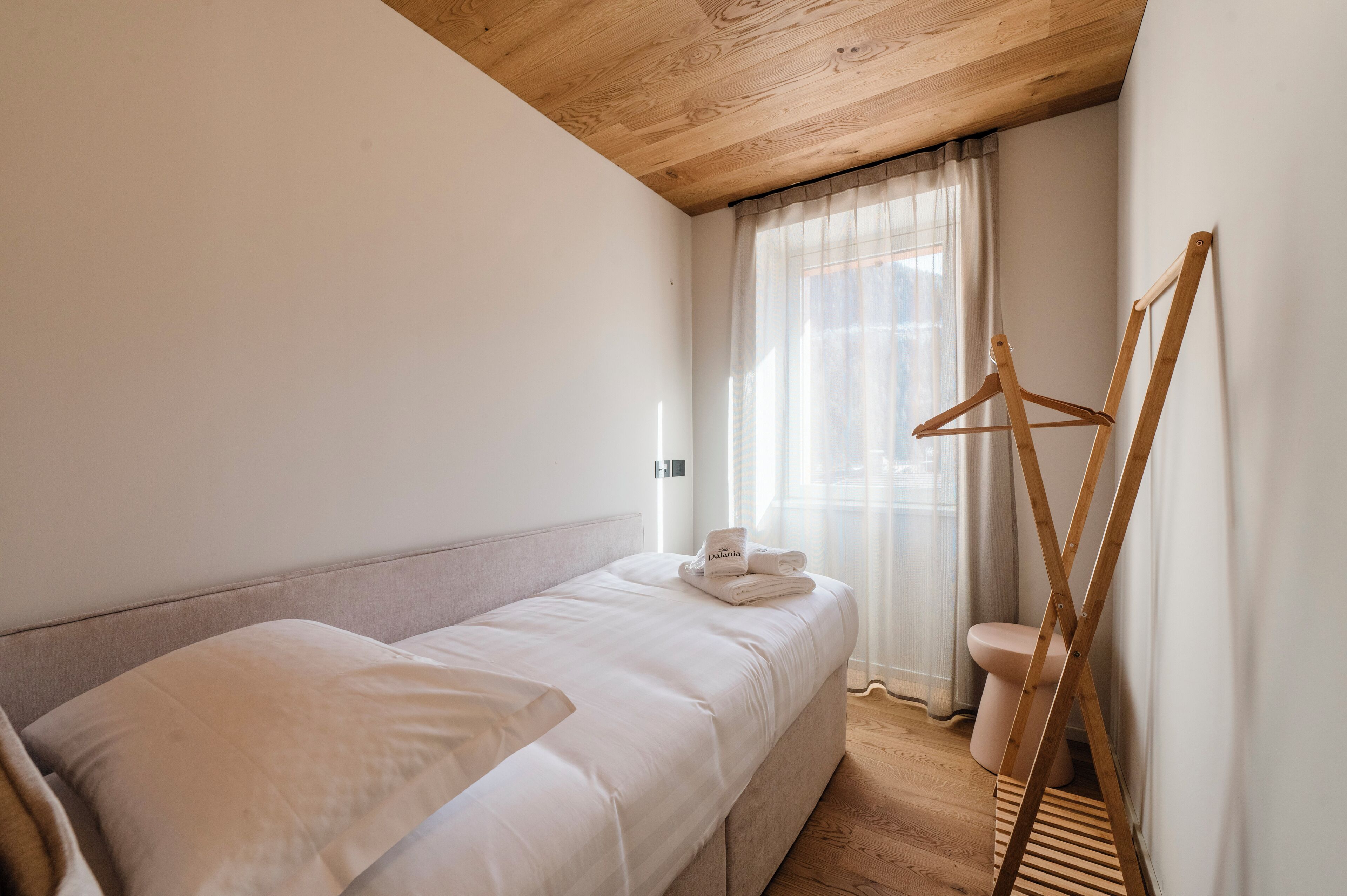 Un dormitorio con una cama, un perchero de madera y un ventanal con cortinas.