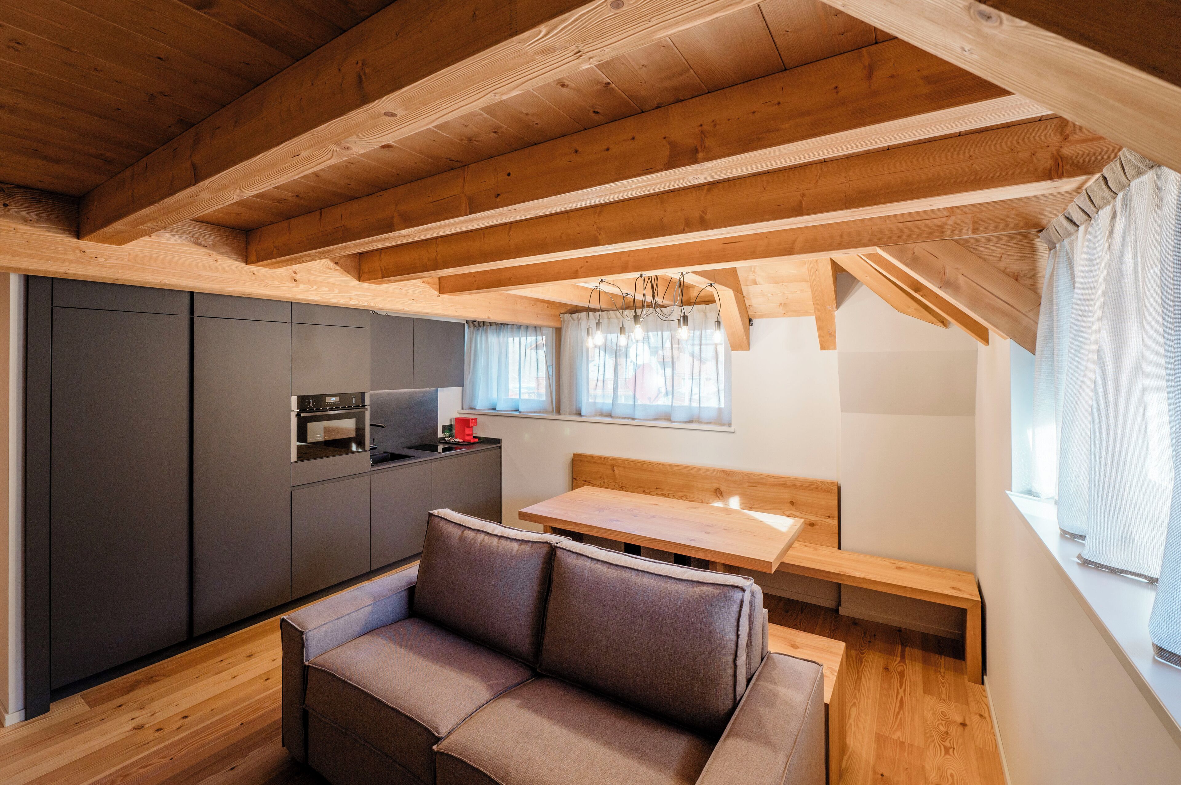 A compact kitchen with dark cabinets, a wooden bench, and a window with curtains.