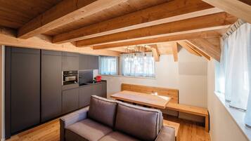 Une cuisine de taille réduite, avec des meubles de couleur sombre, un banc en bois et une fenêtre agrémentée de rideaux.
