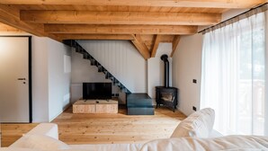 A modern living room with wooden floors, a staircase, a black wood-burning stove, and a large window. - DALANIA MOUNTAIN APARTMENTS (Ponte di Legno)