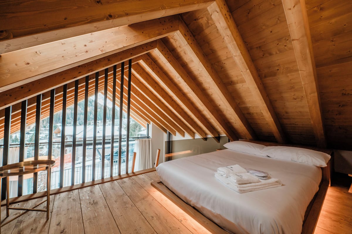 Un dormitorio con techo inclinado, una cama, un ventanal y suelo de madera.