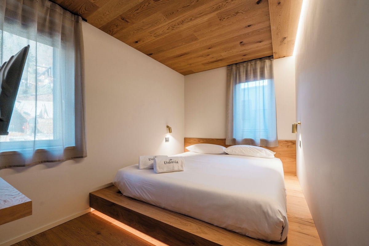 Un dormitorio con techo de madera, una cama con ropa blanca y una mesita de noche con lámpara.