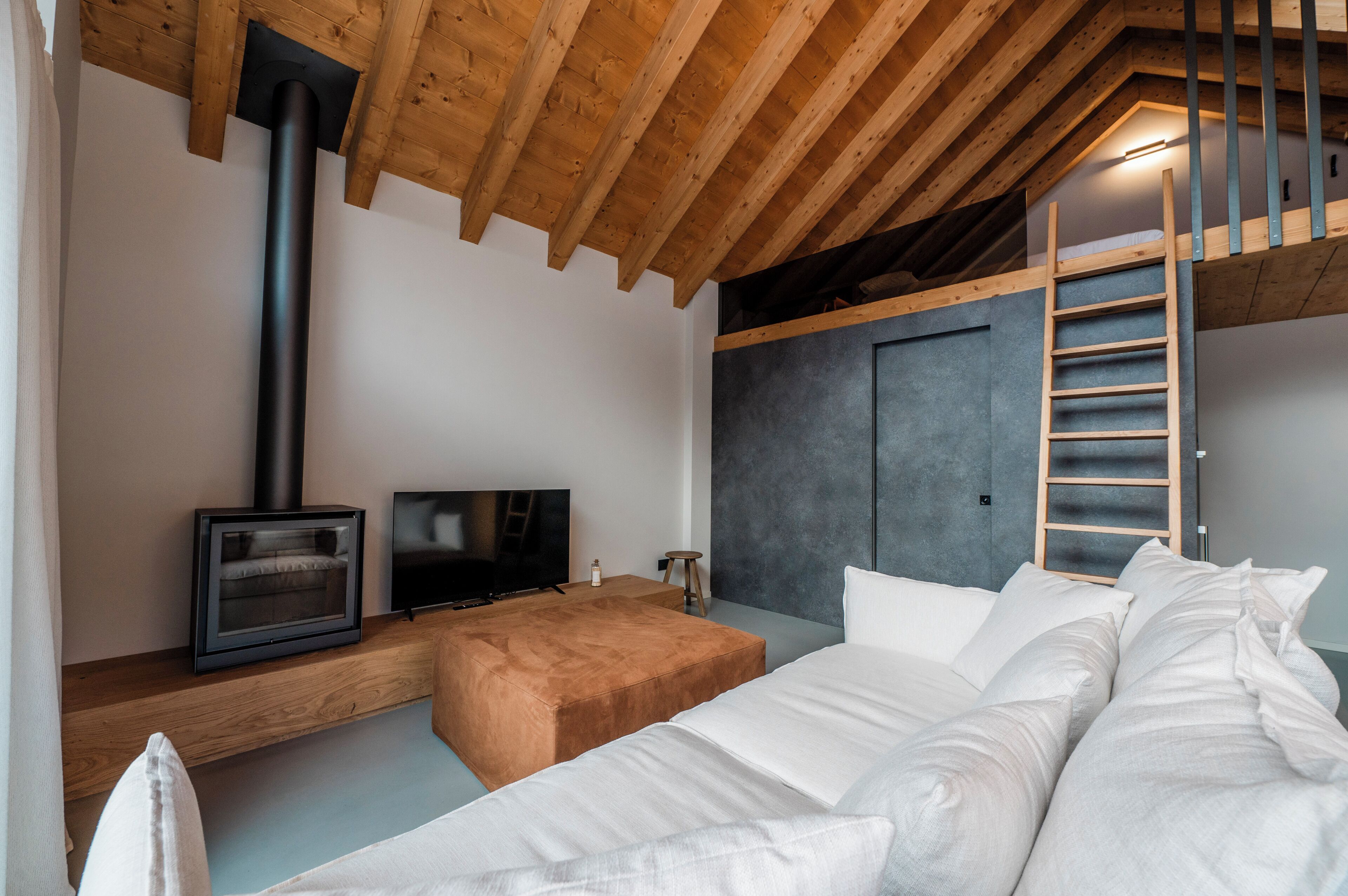 A modern bedroom with a loft-style ceiling, a built-in fireplace, a television, and a comfortable bed.